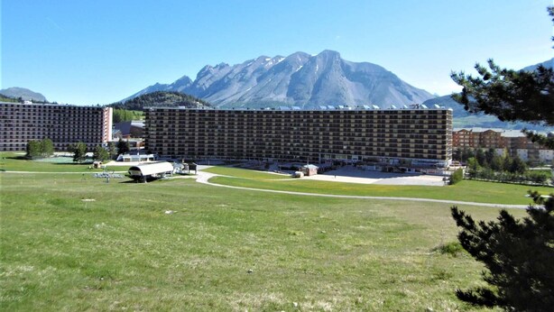 A large hotel with a modern, multi-story structure, surrounded by a grassy field and mountains in the background.