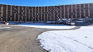 A large, multi-story hotel with a curved facade, a parking area, and a snow-covered ground.