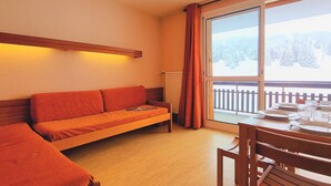 A cozy room with a sofa, a dining table set for two, and a large window with a view of a snowy landscape.