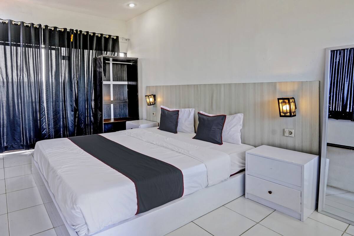 A modern hotel room with a large bed, two bedside tables, a wardrobe, and a mirror.