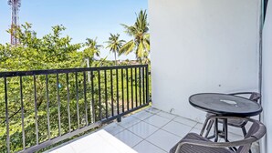 A balcony with a table and chairs, a metal railing, and a view of palm trees and a communication tower. - Capital O 92670 Borobudur Homestay (Banyuwangi)