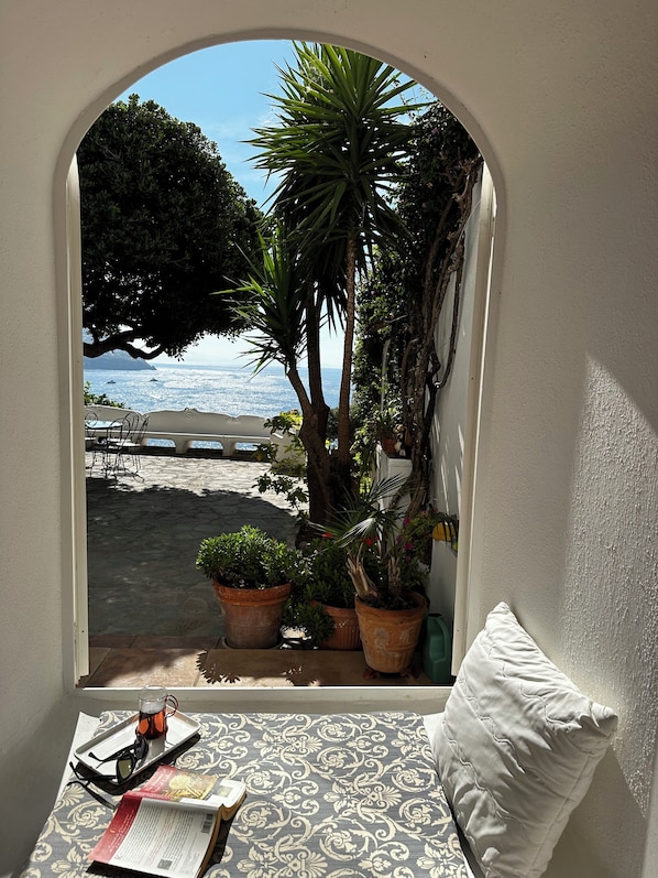 A cozy reading nook with a view of the sea through an arched window, surrounded by potted plants and a white cushion. - Positano, Villa Fornillo 84 is an oasis of peace, tranquility and style (Positano)