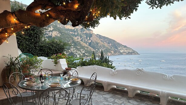 A terrace with a table set for dining, overlooking a coastal view with boats.