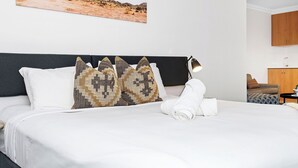 A neatly made bed with white linens, a dark headboard, and patterned pillows. A rolled white towel is placed at the foot of the bed. - Perth's Premier King Deluxe (Perth)