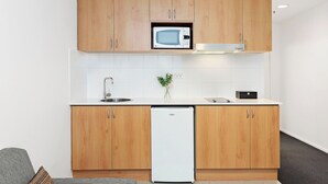 A modern kitchen with wooden cabinets, a built-in microwave, a dishwasher, and a small plant on the counter. - Perth's Premier King Deluxe (Perth)