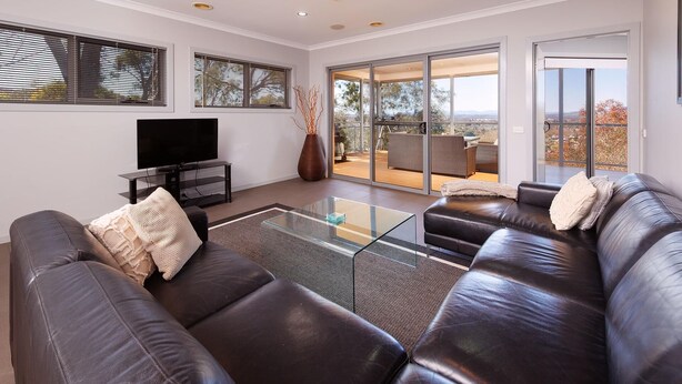A modern living room with a leather sofa, a glass coffee table, and a flat-screen TV. - Divine Views on Roper - Glorious three bedroom, two bathroom townhouse with views to die for! (Albury)