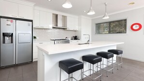 A modern kitchen with a central island, bar stools, a refrigerator, and a coffee machine. - Divine Views on Roper - Glorious three bedroom, two bathroom townhouse with views to die for! (Albury)