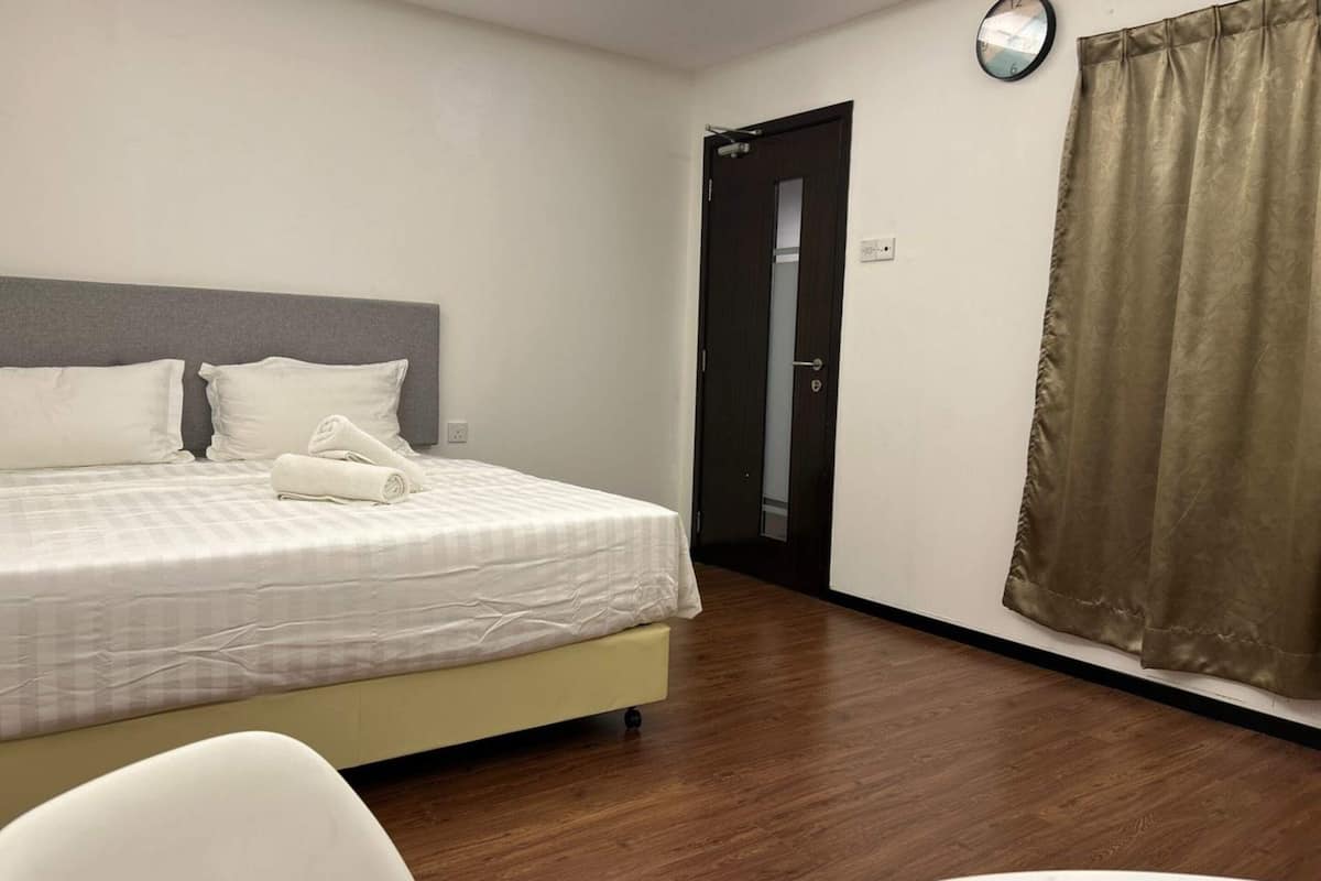 A hotel room with a bed, a chair, a door, and a curtain.