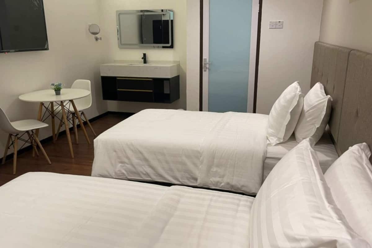 A hotel room with two beds, a small desk with a chair, a sink, and a mirror.