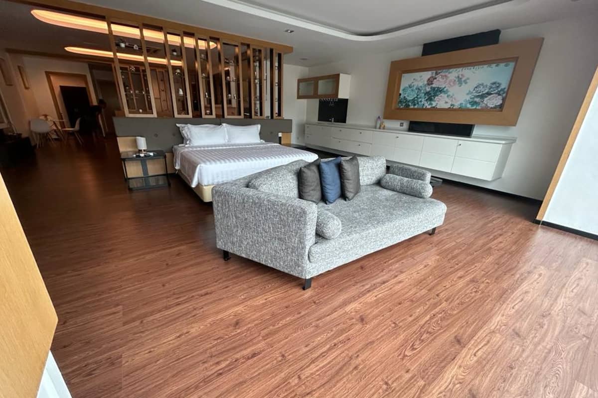 A modern hotel room with a large bed, a grey sofa, a TV, and a painting on the wall.