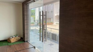 Une pièce moderne dotée d’une porte vitrée donnant sur un espace extérieur, d’un banc en bois agrémenté de plantes et d’un sol carrelé.