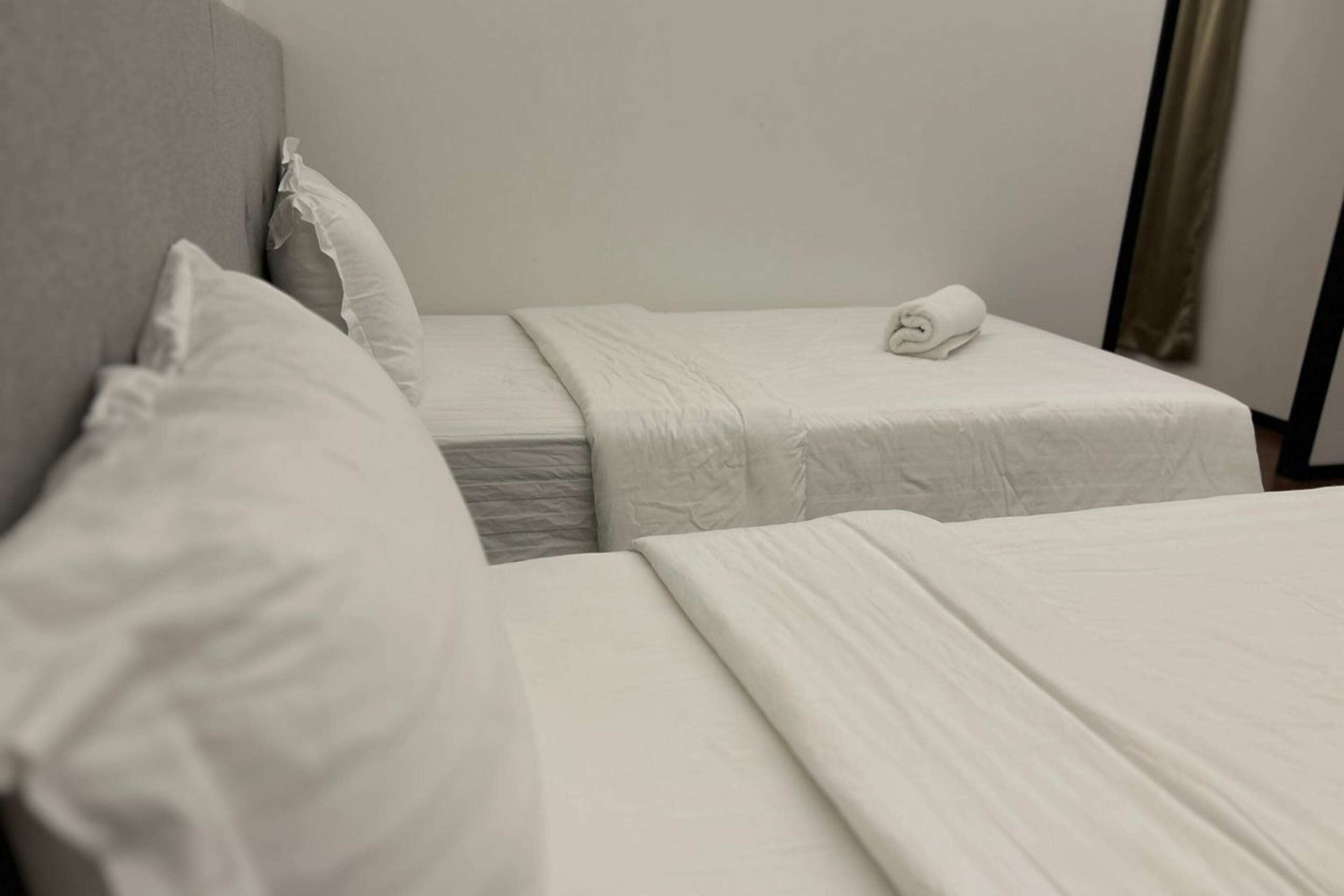 Una habitación de hotel con dos camas individuales, cada una con una almohada y una toalla doblada.