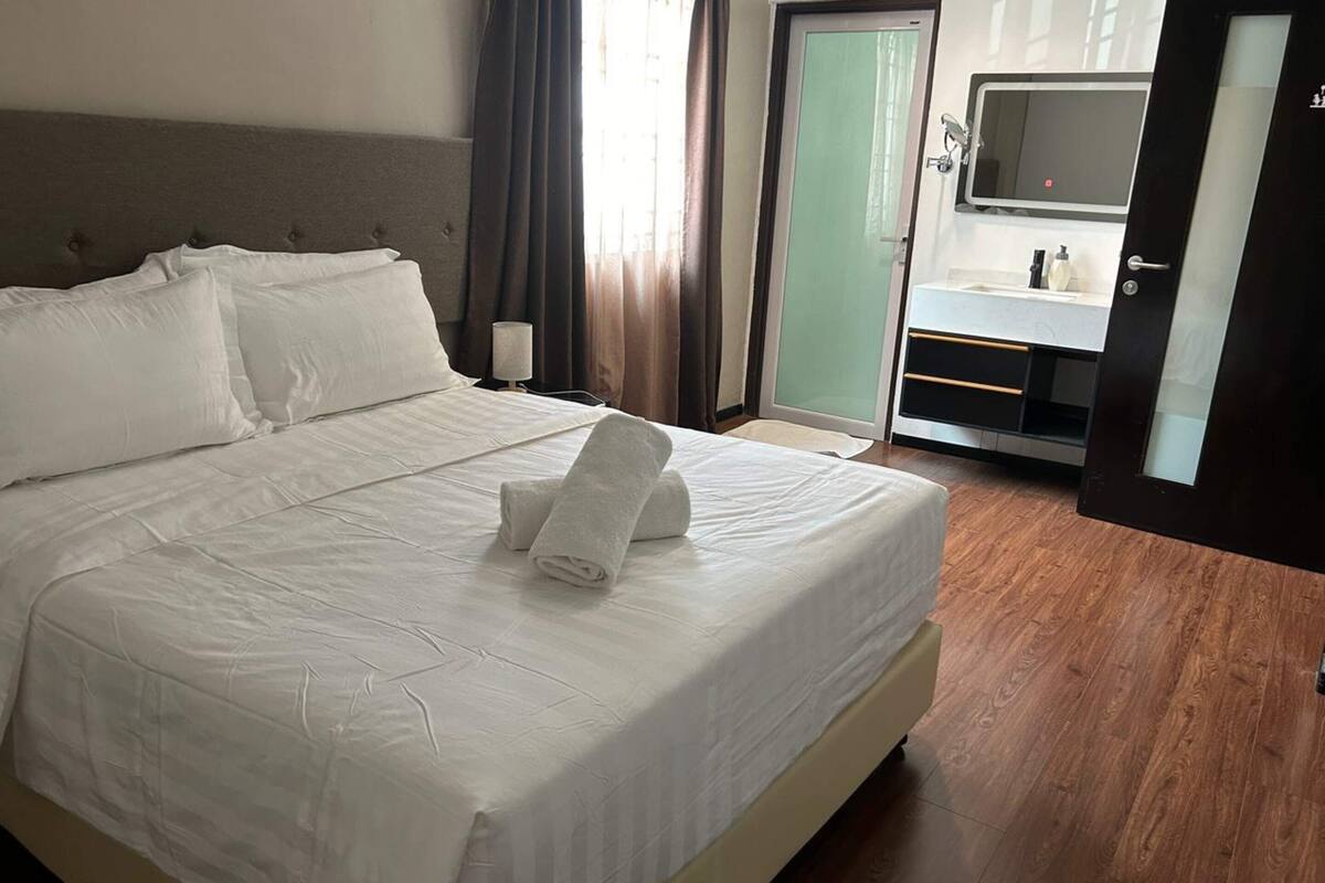 A hotel room with a large bed, a bedside table, a mirror, and a bathroom with a sink and mirror.
