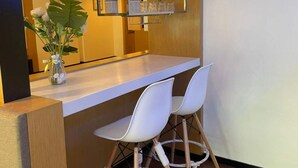 Un espace bar moderne avec un comptoir en bois, deux tabourets de bar blancs et un grand miroir.