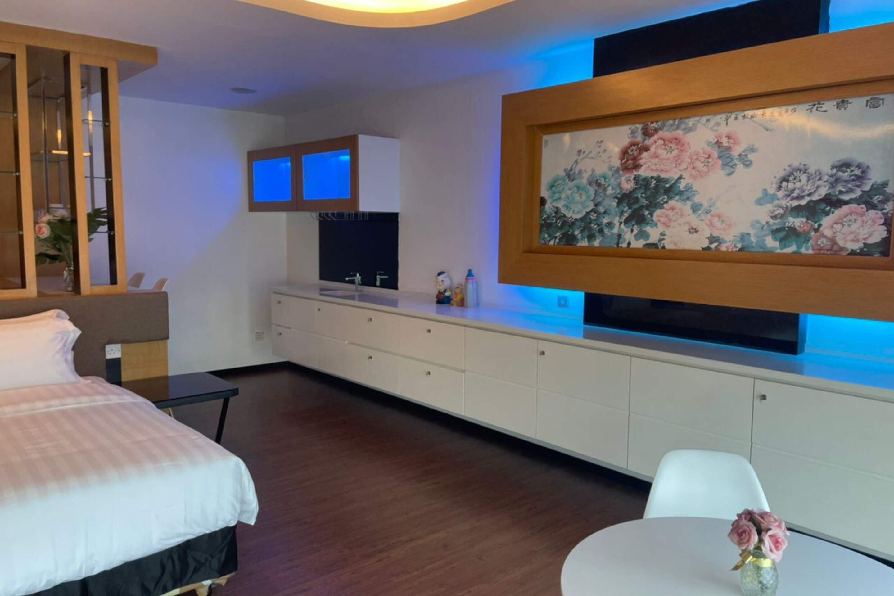 A modern hotel room with a bed, a desk, a TV, and a painting on the wall.