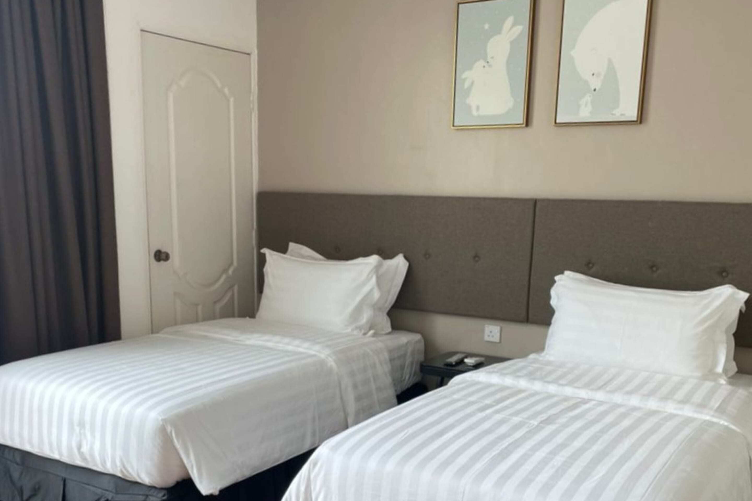 A hotel room with two beds, a headboard, a nightstand, and two framed pictures on the wall.