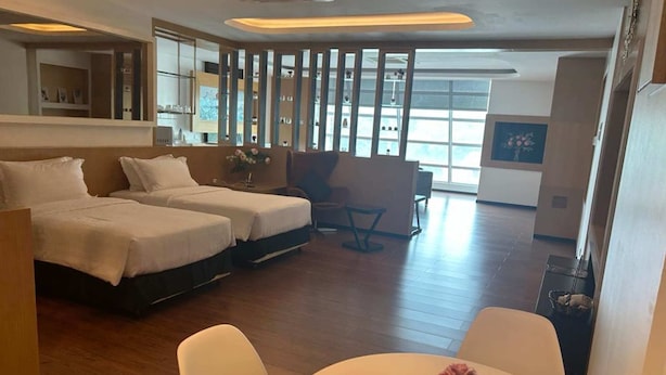 Une chambre d’hôtel avec deux lits, un coin salon avec une table et des chaises, une grande fenêtre et un vase décoratif posé sur la table.