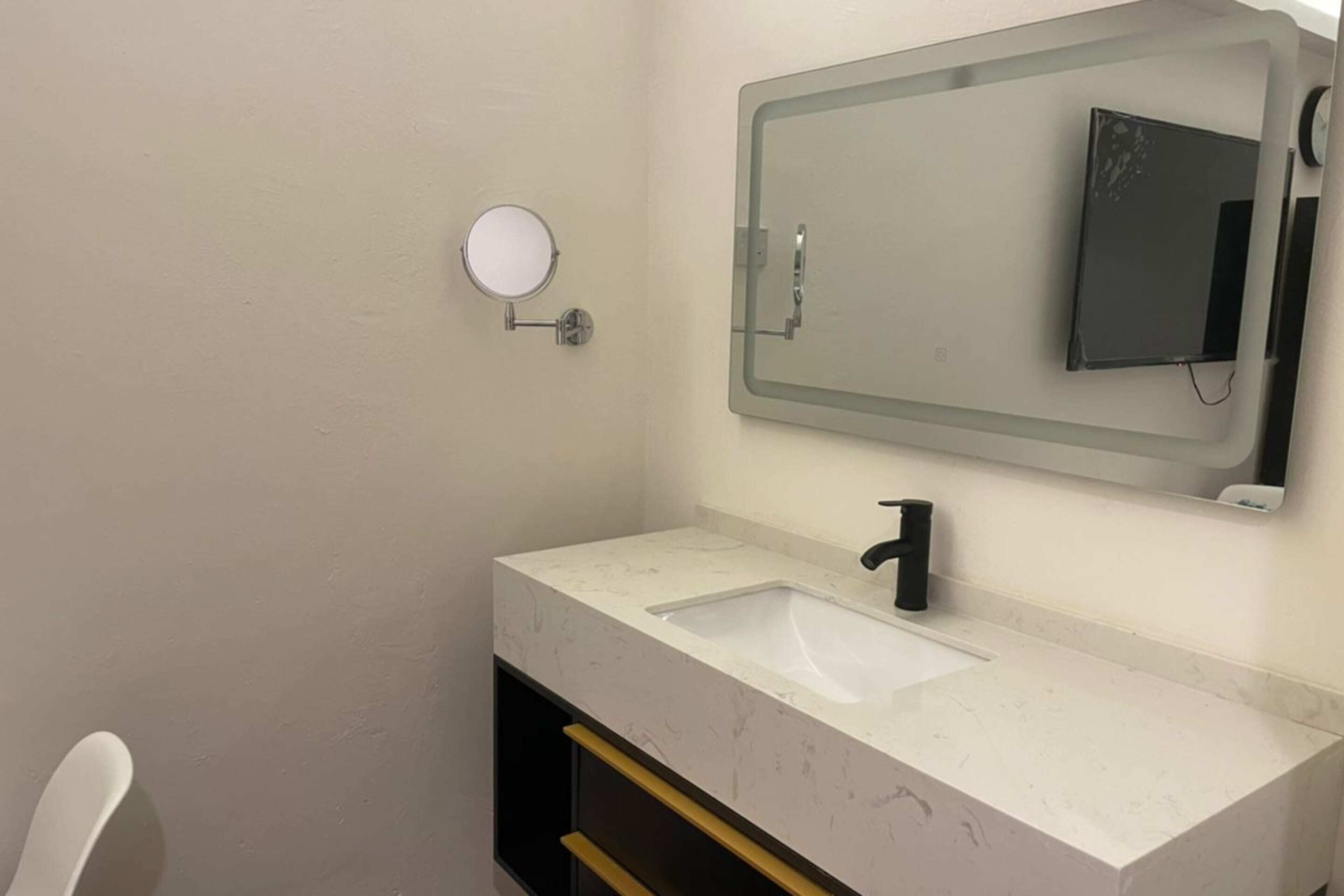 A bathroom with a white sink, a mirror, and a round mirror on the wall.