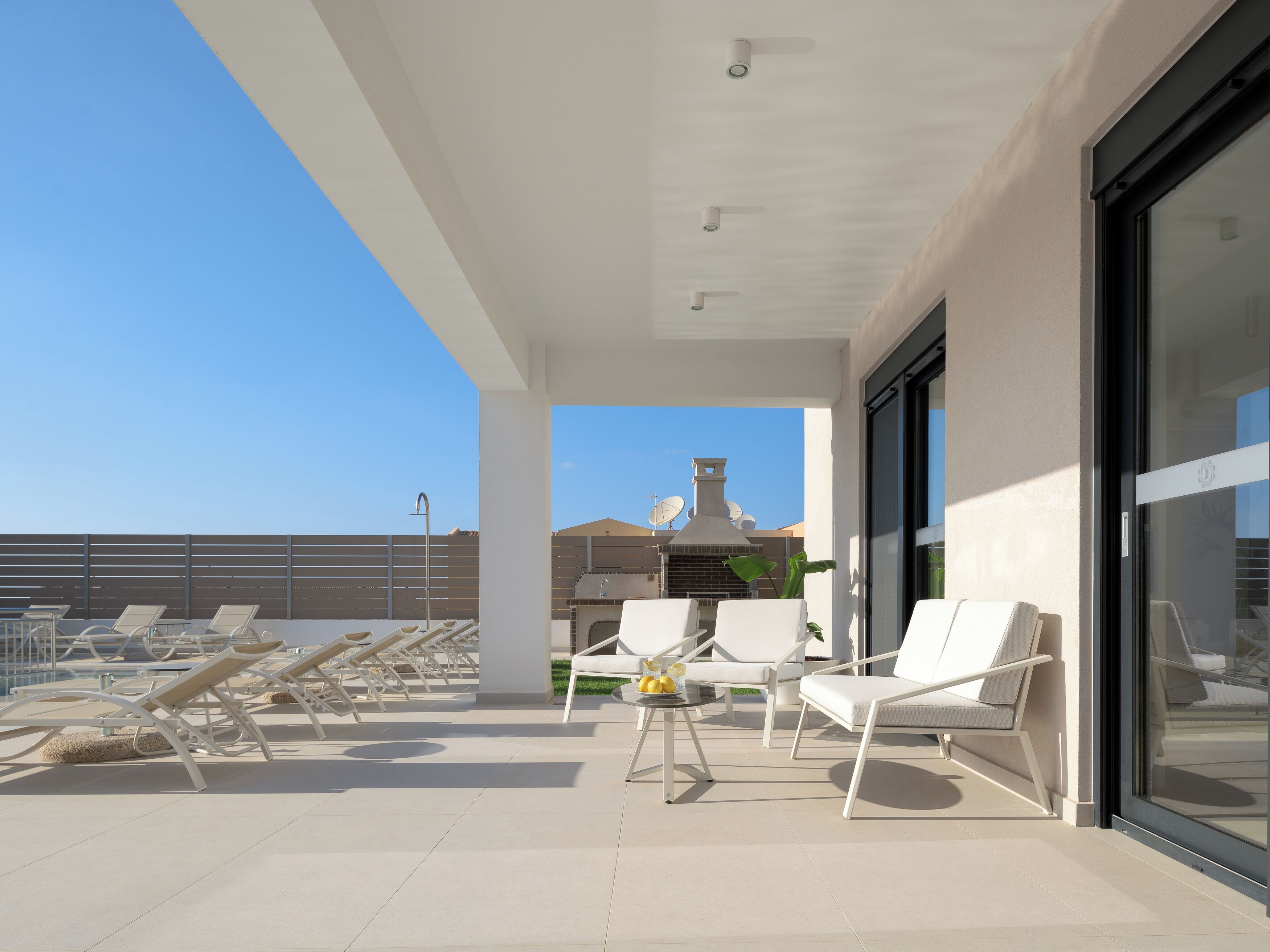 Eine moderne Außenpatio mit weißen Lounge-Stühlen, einem Tisch mit Zitronen und einem Grill.