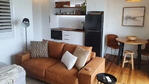 Ein kompakter Wohnraum mit einer Couch, einem Esstisch mit Stühlen, einer Küchenzeile inklusive Schränken und Geräten sowie einer Stehlampe.