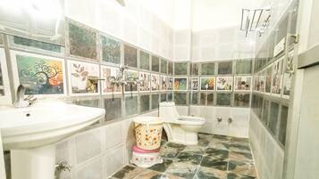 Un baño con lavabo, inodoro y ducha. Las paredes están cubiertas de azulejos con diseños florales.