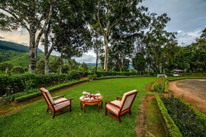A lush garden with a dining table set for two, surrounded by chairs, and a bench in the background. - Lockhart Bungalow Munnar CGH Earth (Devikolam)