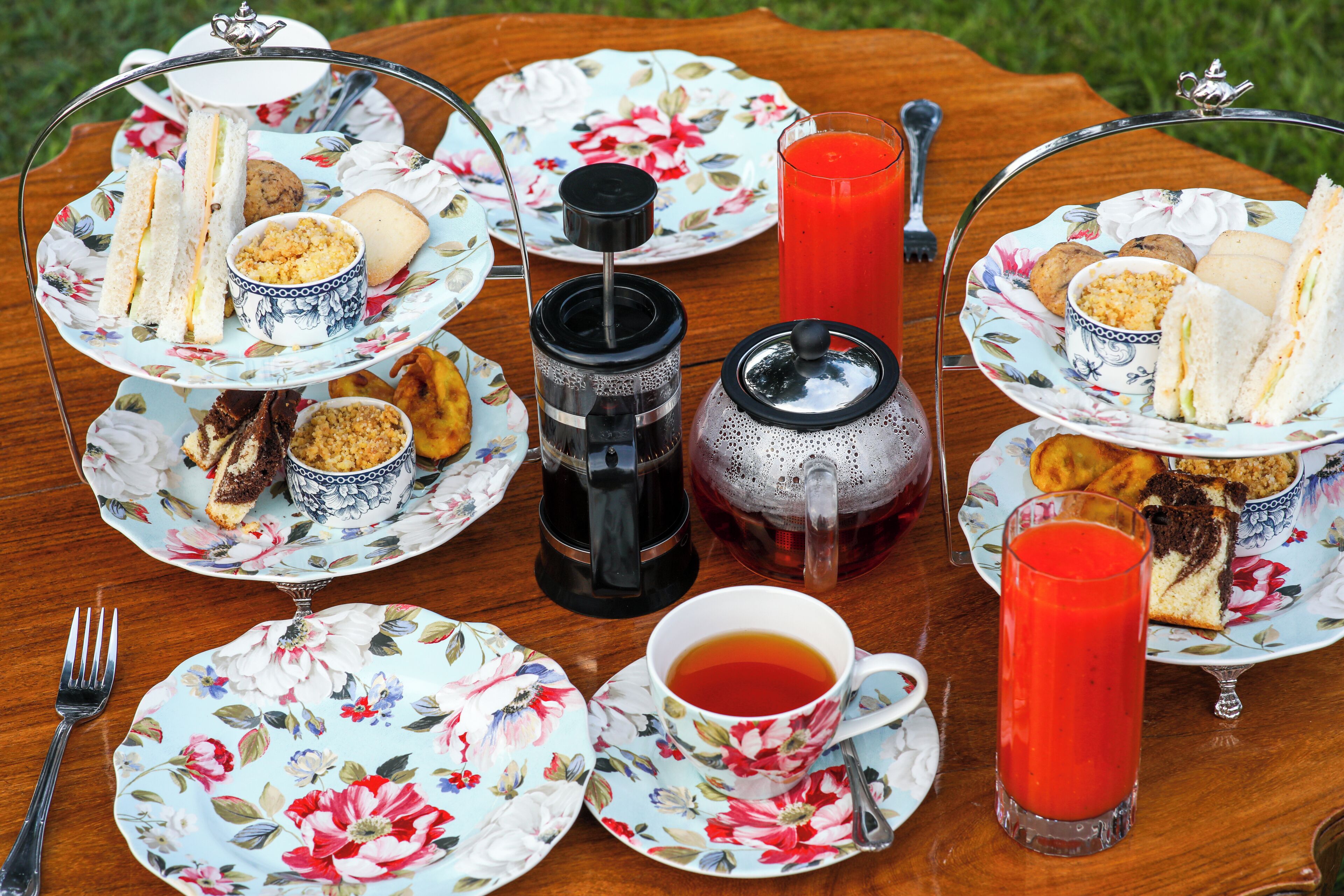 A table set with floral-patterned plates, sandwiches, cookies, and a teapot.
