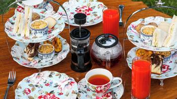 A table set with floral-patterned plates, sandwiches, cookies, and a teapot.