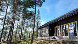 Eine moderne Hütte mit großen Fenstern, umgeben von hohen Bäumen und einer grünen Wiese.