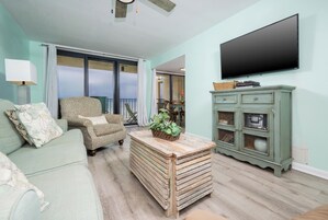 A living room with a sofa, armchair, wooden coffee table, and a television on the wall.