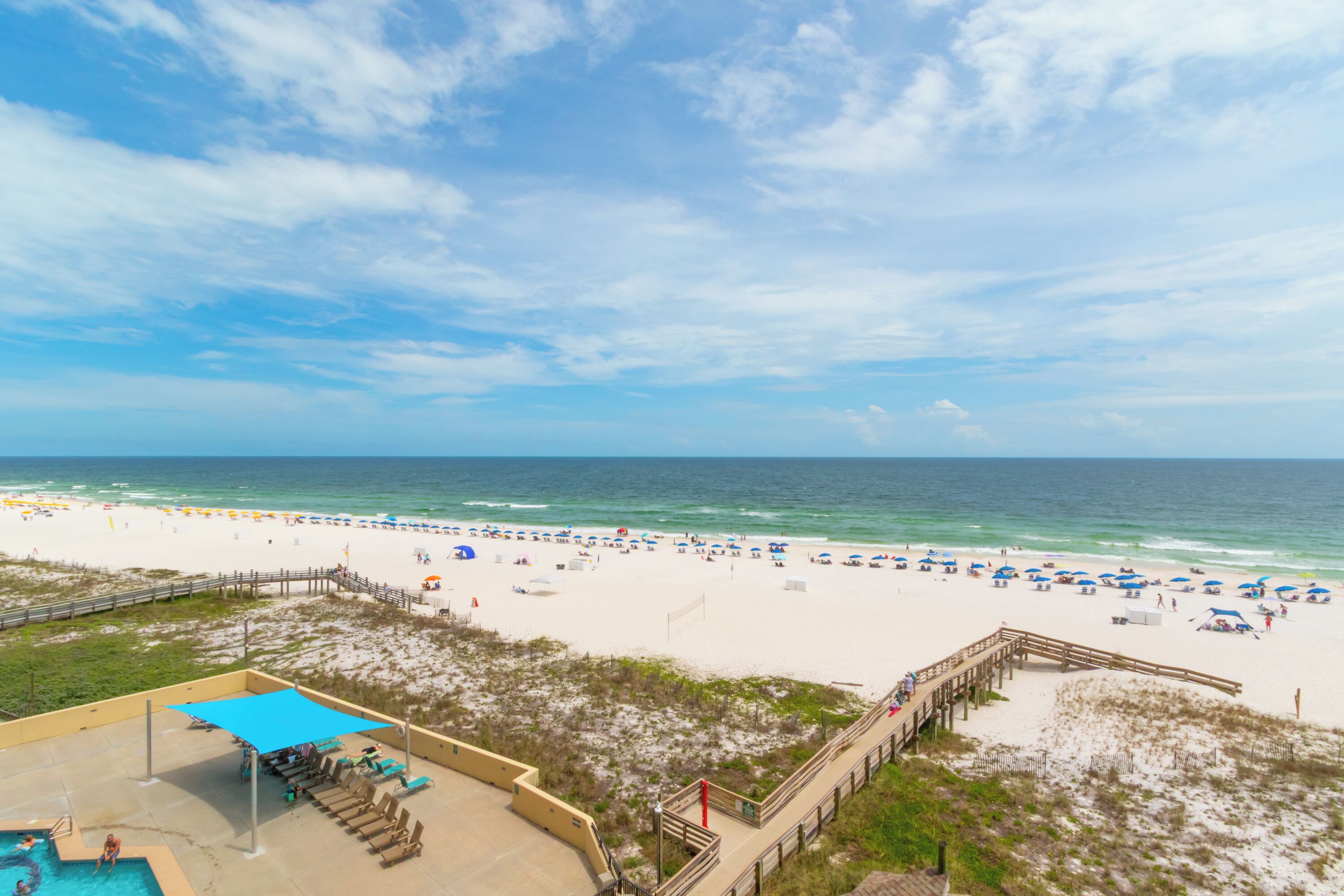 A beach view with a wooden deck and a pool area.
