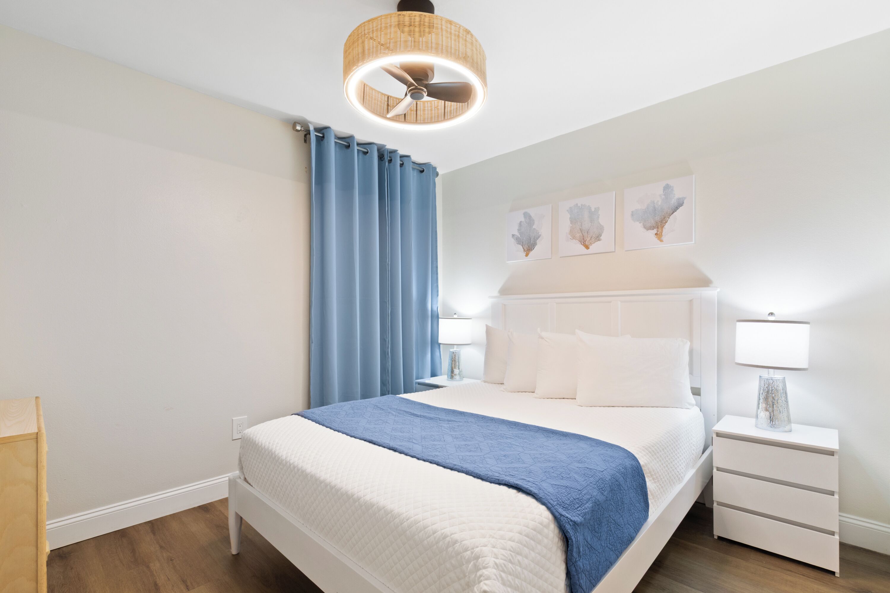 A bedroom with a bed, nightstands, a lamp, a ceiling fan, and artwork on the wall.
