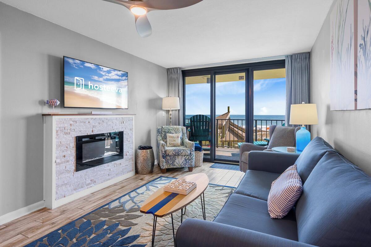 A modern living room with a fireplace, a flat-screen TV, a sofa, and a balcony with a view.