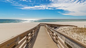 A wooden boardwalk leading to a beach with a clear sky and sunlight reflecting on the water.