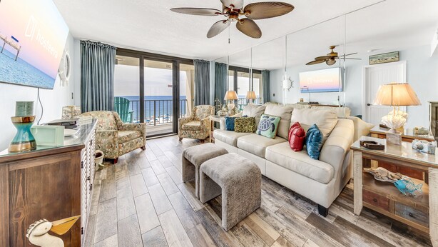 A spacious living room with a large window, a ceiling fan, and a television displaying a scenic view.