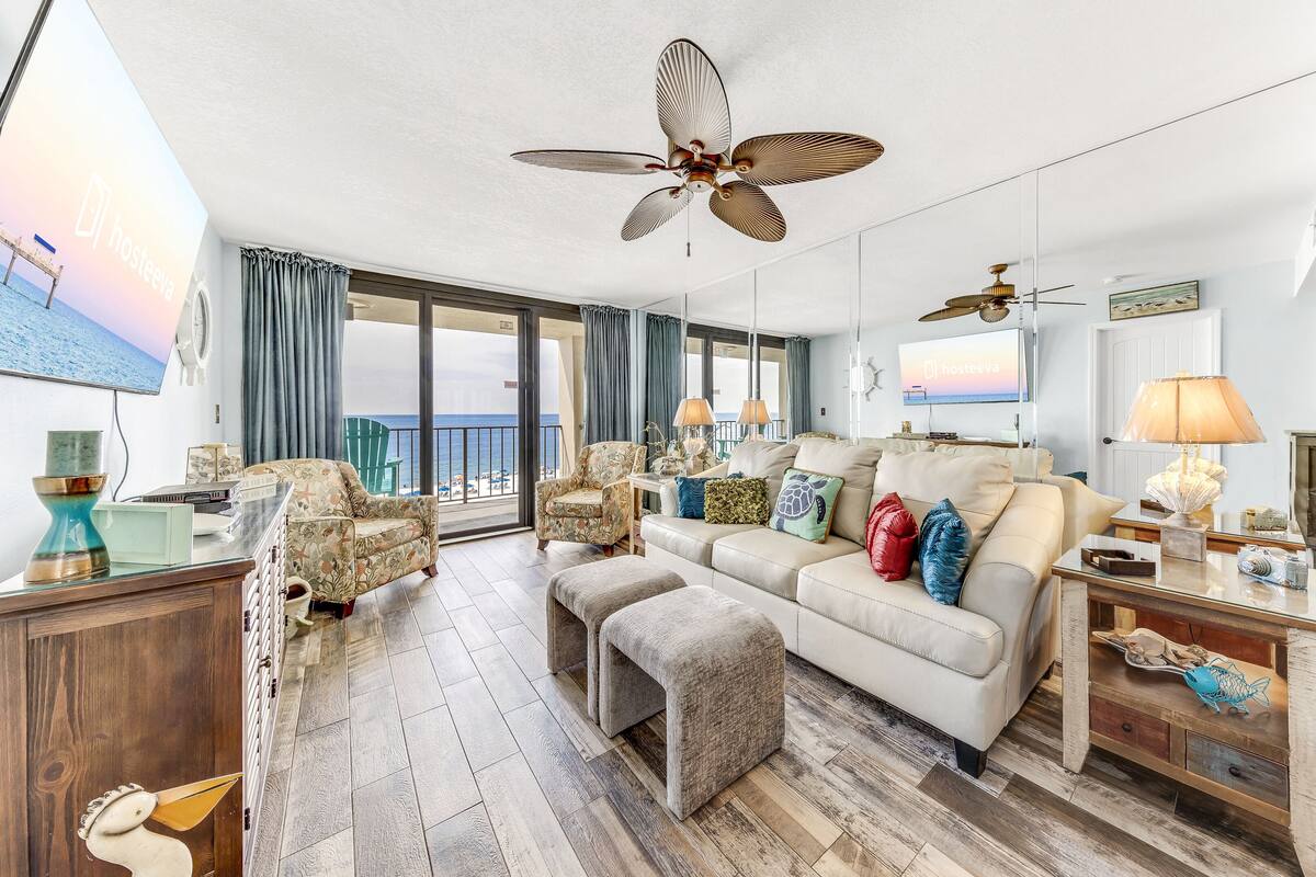A spacious living room with a large window, a ceiling fan, and a television displaying a scenic view.