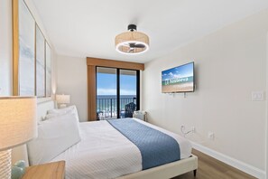 A hotel room with a bed, a television, a view of the beach, and a balcony.