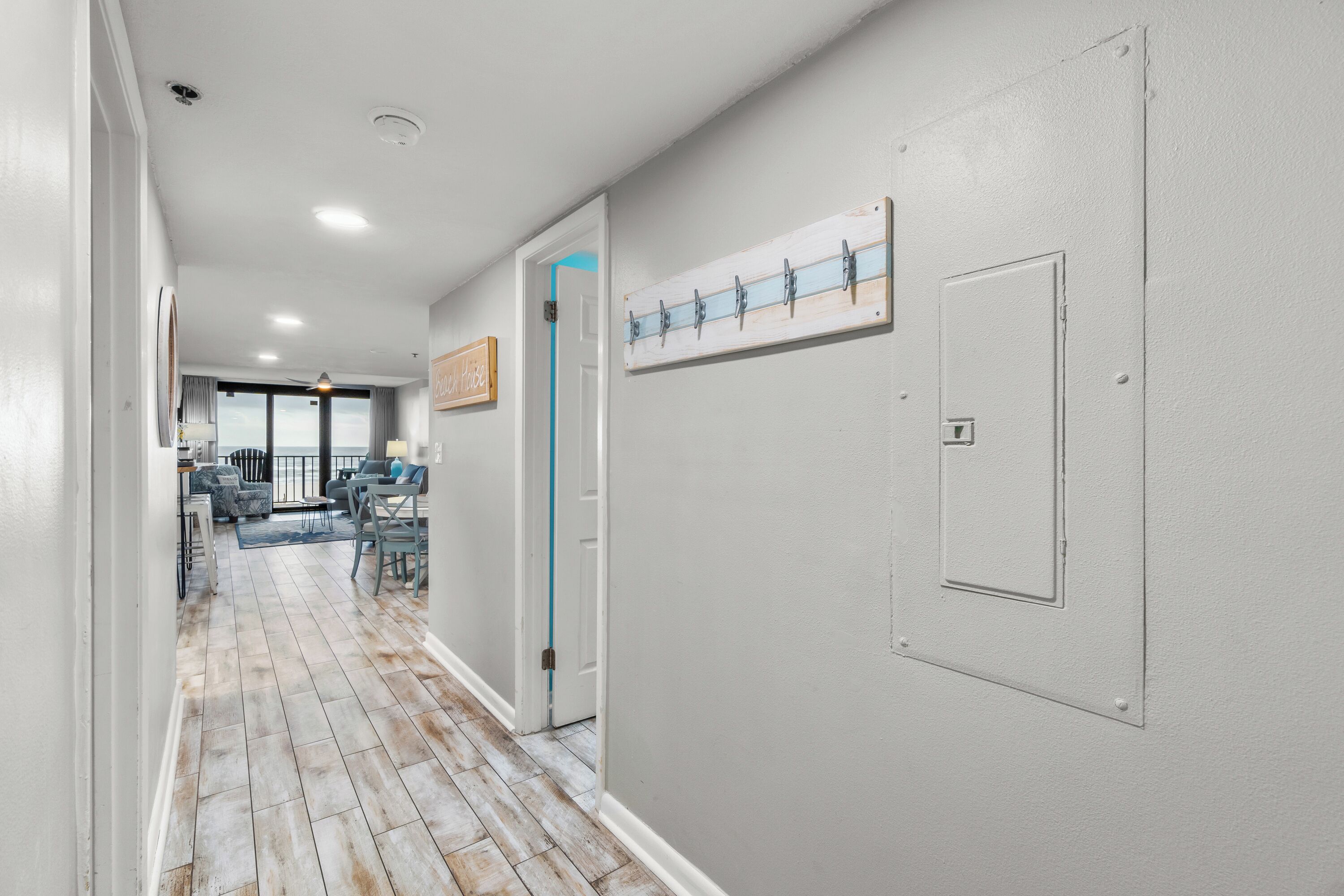 A hallway with a wooden floor, a door with a blue handle, and a wall-mounted light switch.