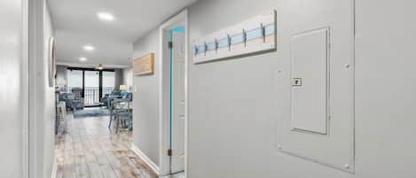 A hallway with a wooden floor, a door with a blue handle, and a wall-mounted light switch.