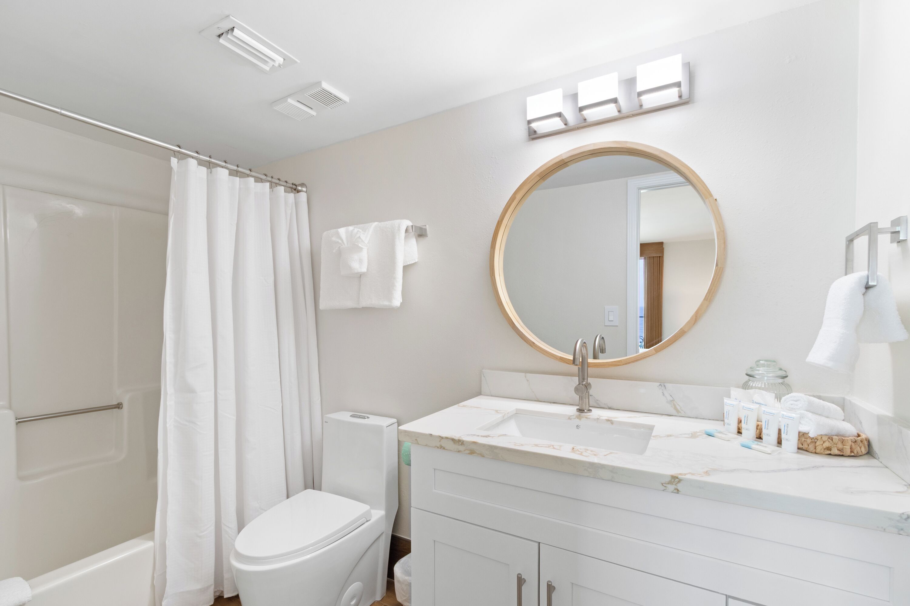 A modern bathroom with a toilet, sink, shower, and a round mirror.