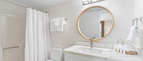 A modern bathroom with a toilet, sink, shower, and a round mirror.