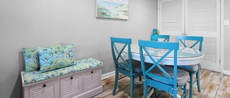A dining area with a table and chairs, a bench with patterned cushions, and a painting on the wall.
