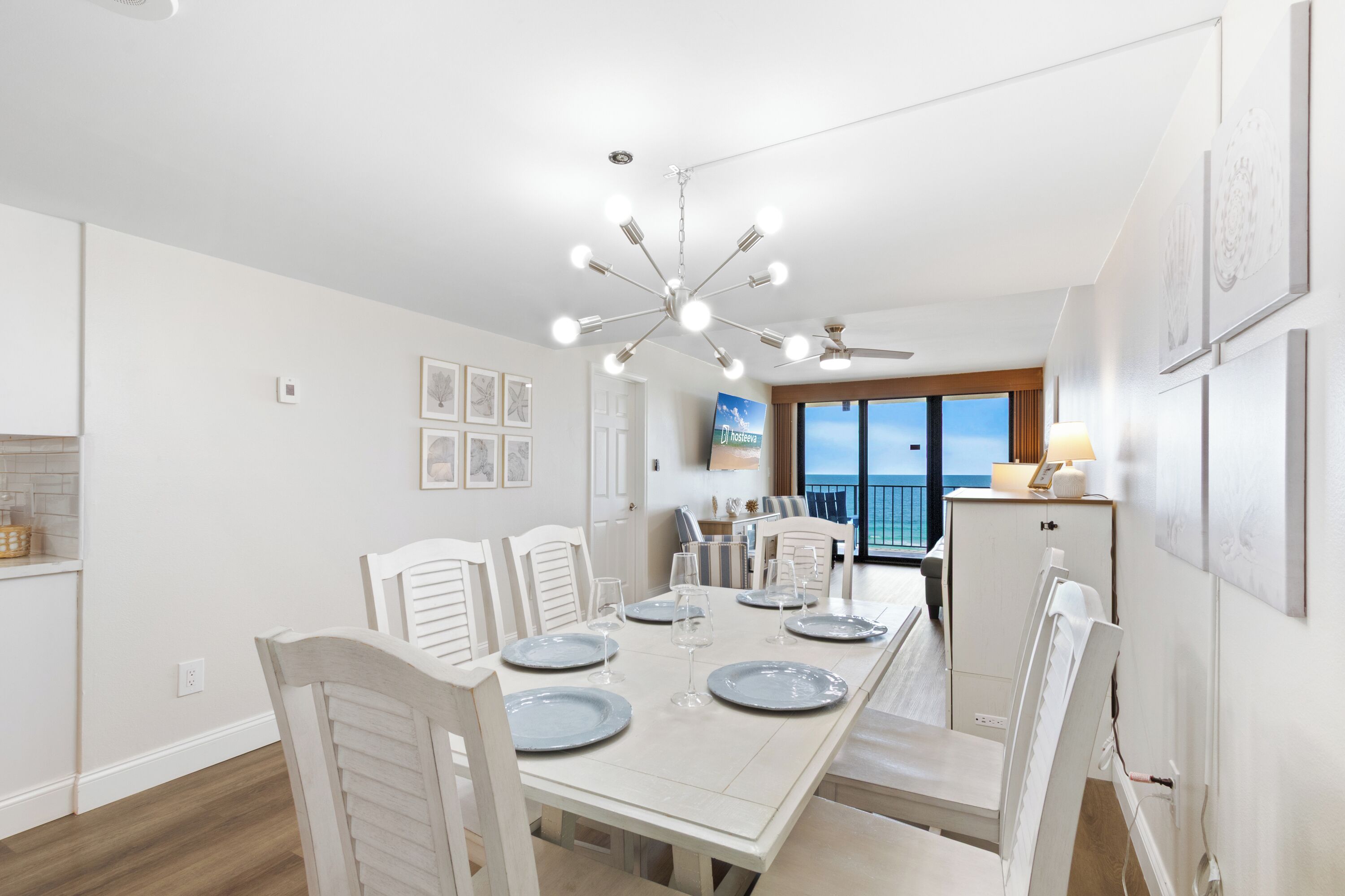 Un coin repas avec une table blanche dressée pour six personnes, un ventilateur de plafond et une vue sur l’océan.