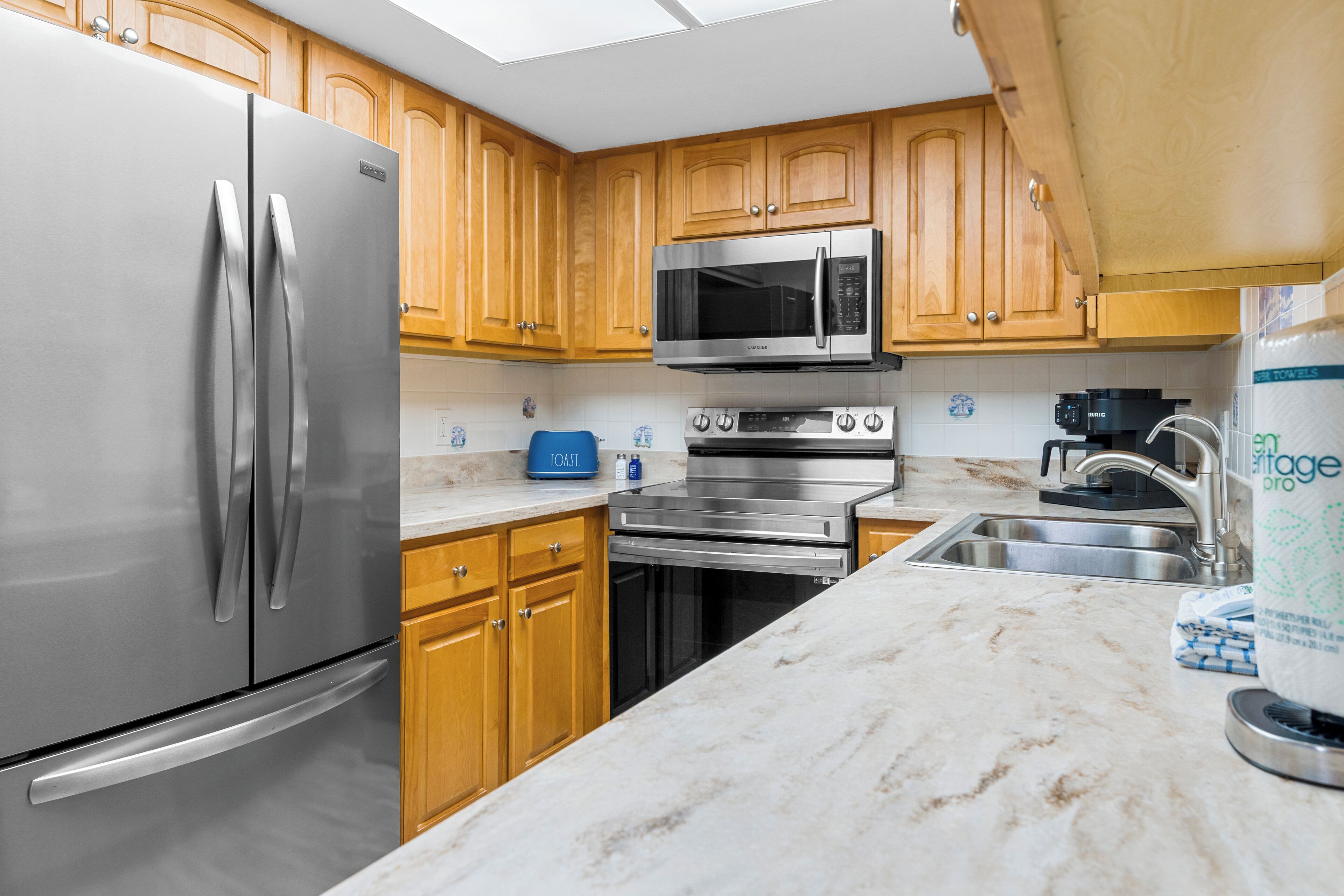 A kitchen with stainless steel appliances, wooden cabinets, a toaster, and a sink.