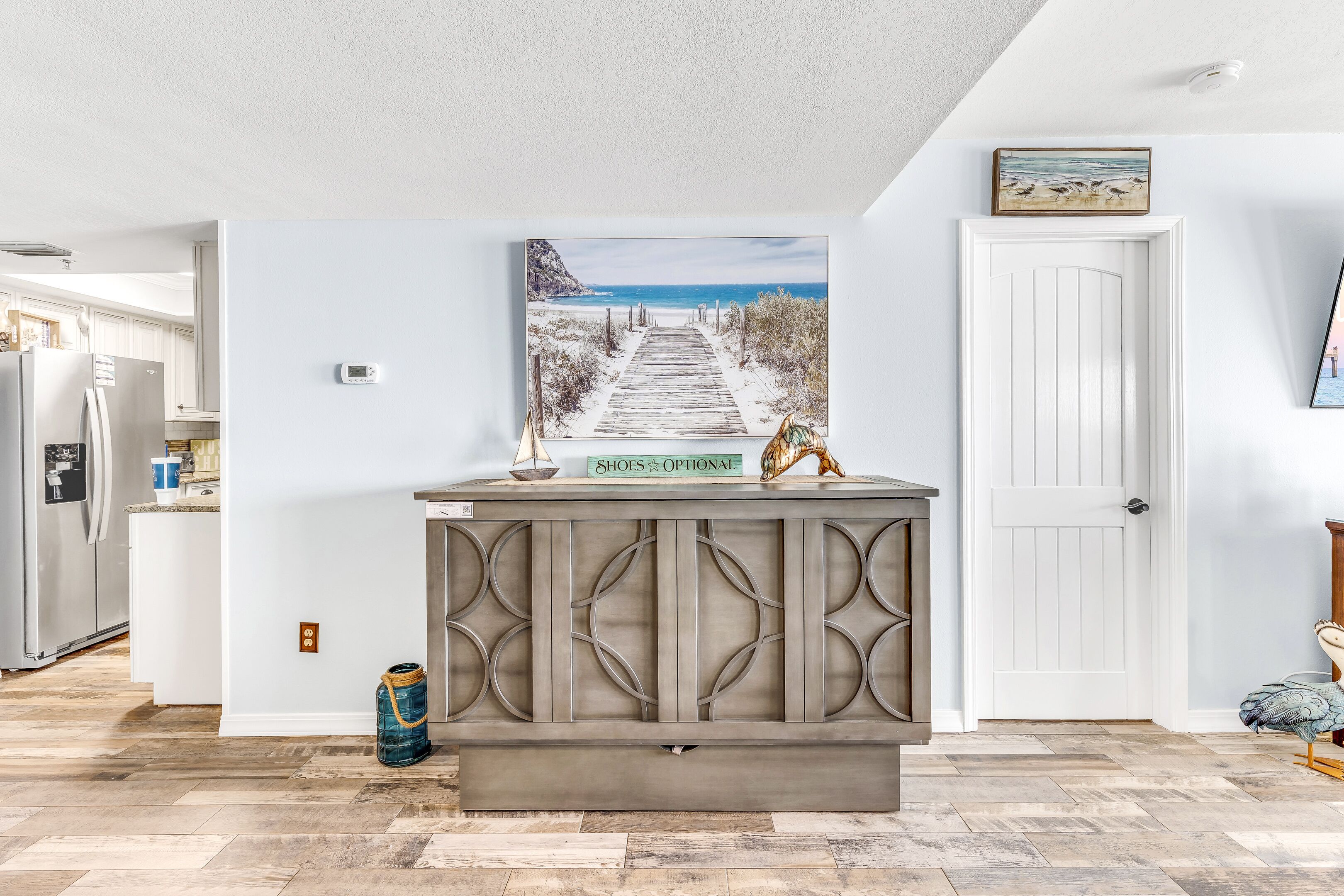 A kitchen with white cabinets, a wooden island with decorative panels, and a painting of a beach scene above it.