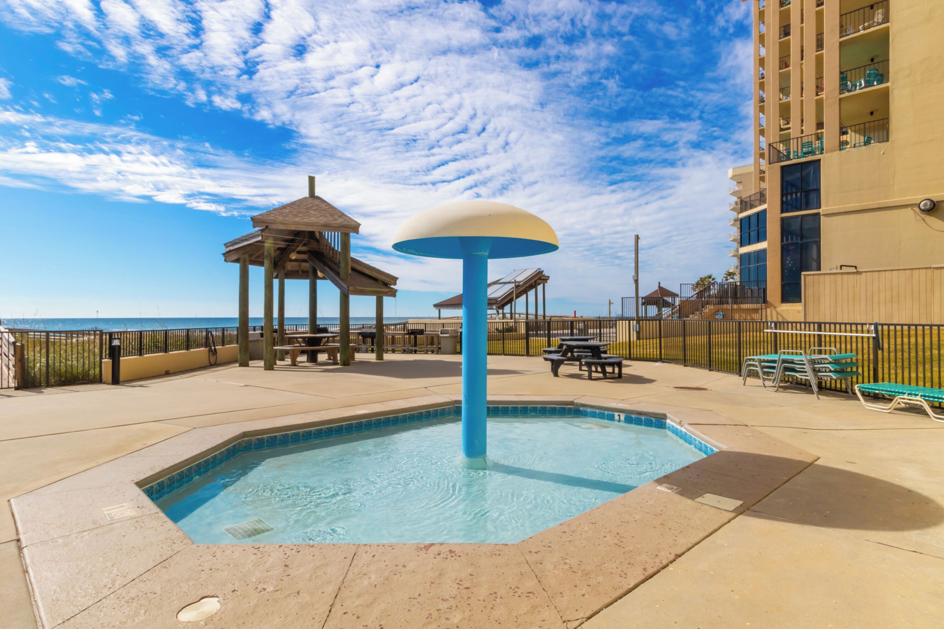 A swimming pool with a blue and white structure in the center, surrounded by a deck with benches and a fence.
