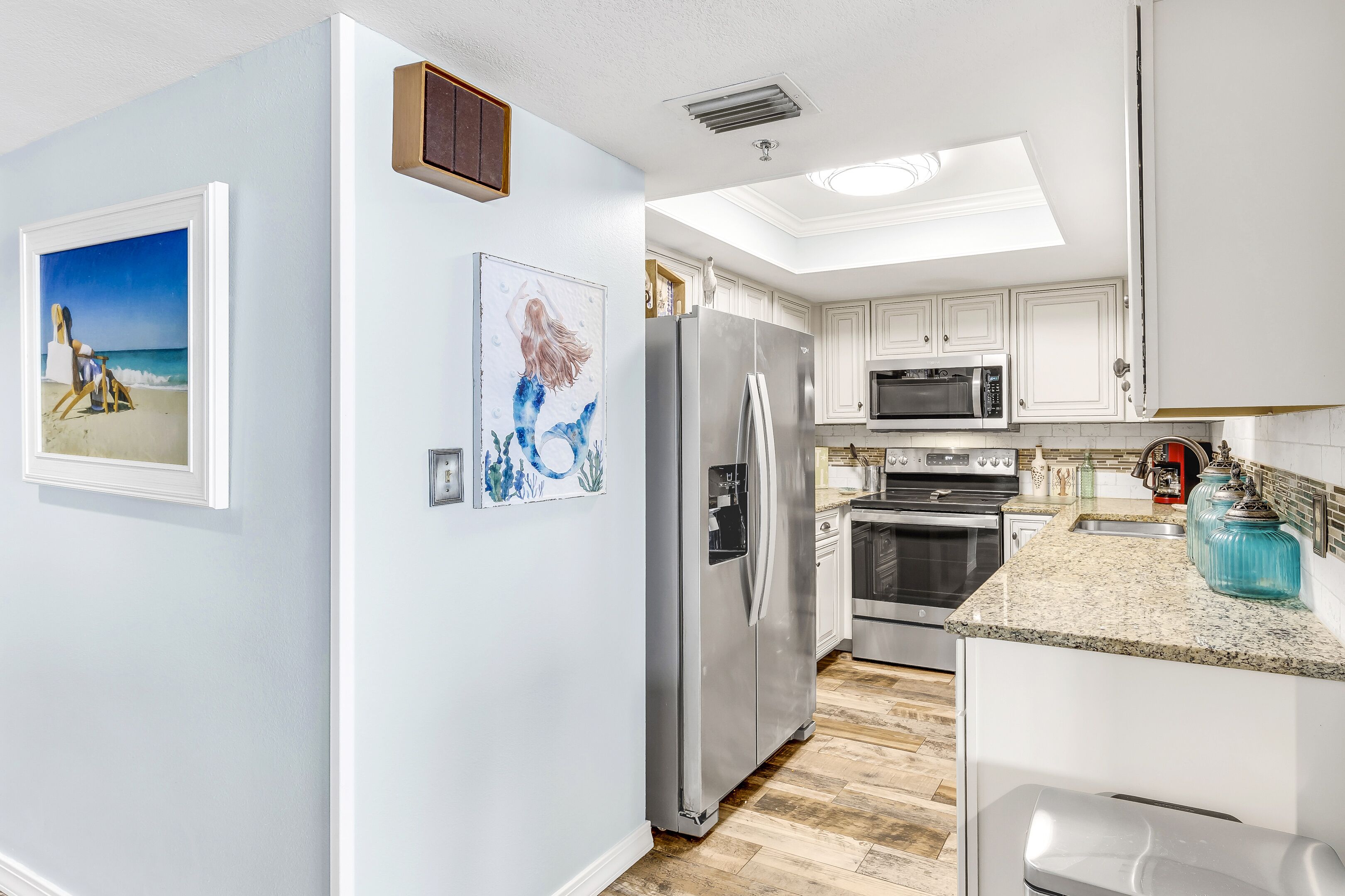 A modern kitchen with white cabinets, stainless steel appliances, and artwork on the walls.