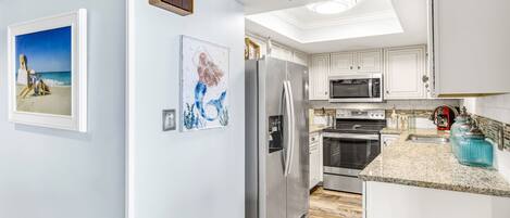 A modern kitchen with white cabinets, stainless steel appliances, and artwork on the walls.