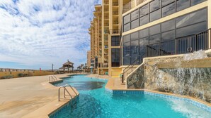 A swimming pool area with a waterfall feature, surrounded by a multi-story building with balconies.