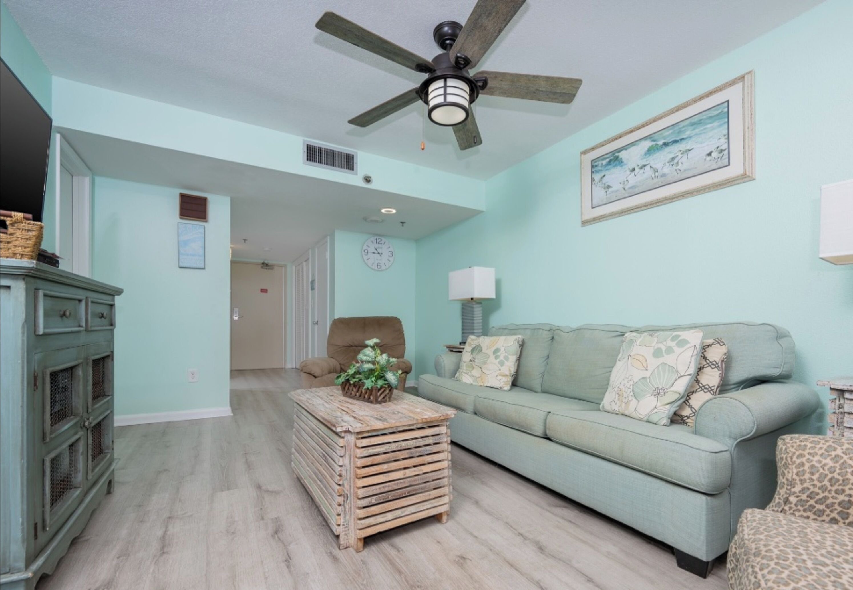 A living room with a light blue wall, a ceiling fan, a sofa, a coffee table, and a cabinet.